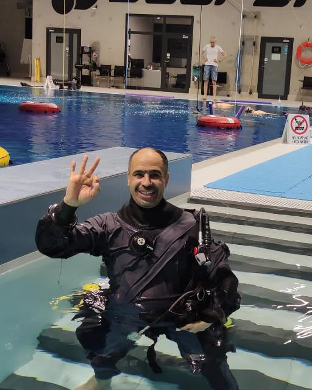 Waleed Rashed w suchym skafandrze na basenie Deepspot pokazuje gest OK